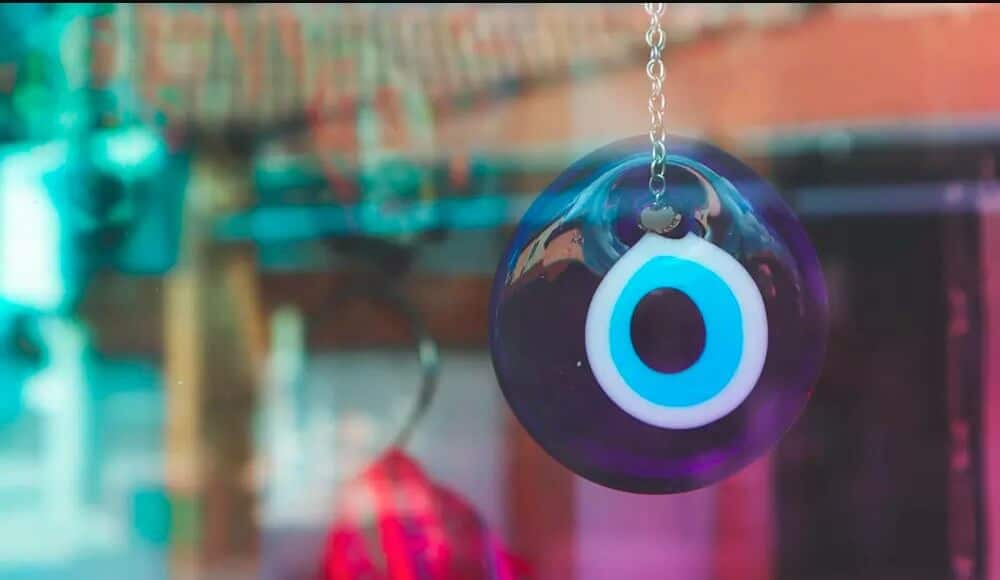 Evil eye meaning, a round blue and white glass pendant hanging on a chain.