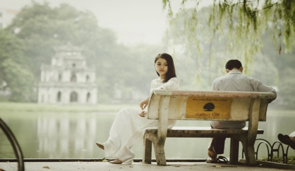 Break a love spell, woman and man sitting on a bench in front of a pond.