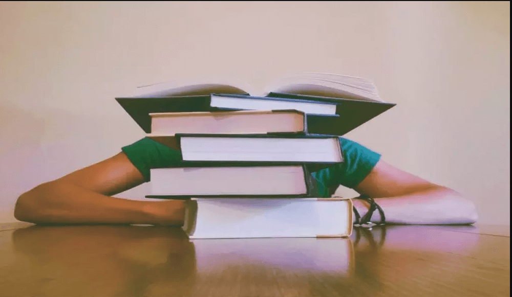 Black magic symptoms, female hiding behind a big stack of books on a table.