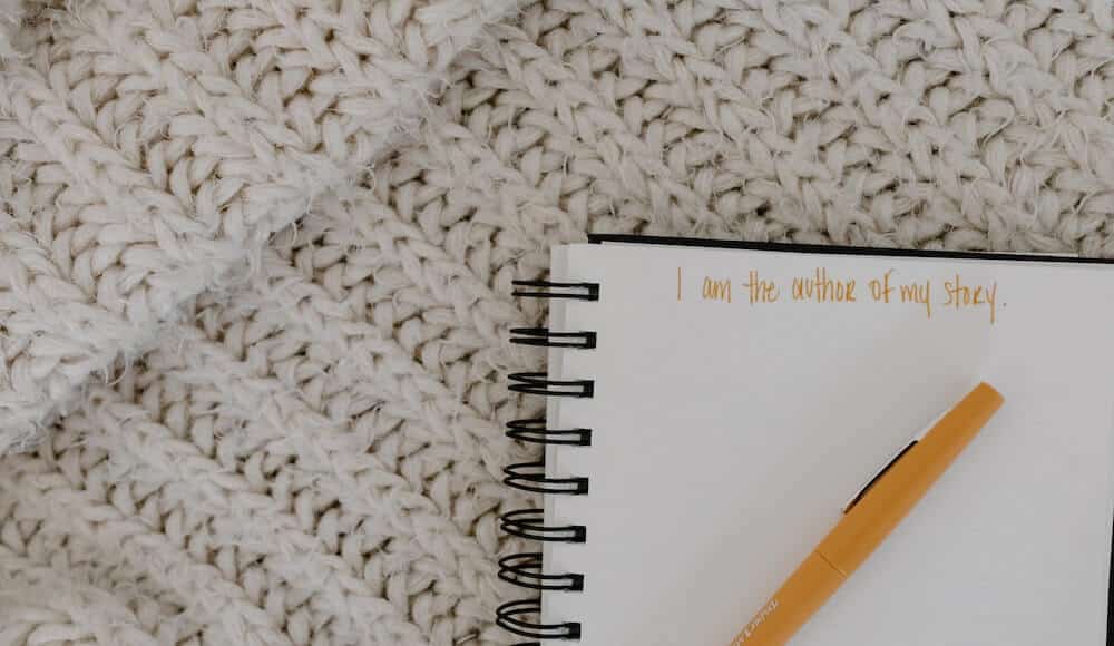 Spiritual affirmations, notebook on a braided white blanket with orange pen.