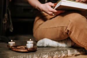 Woman sitting reading a book next to candles doing a spiritual house cleanse.