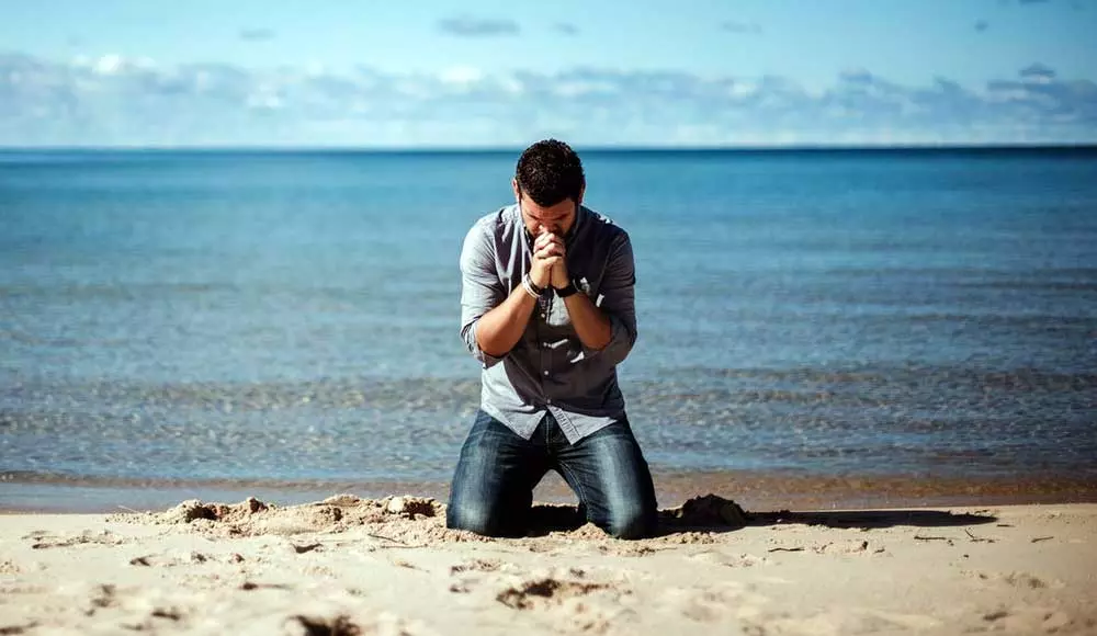 Prayer of healing, man praying on a beach on his knees.