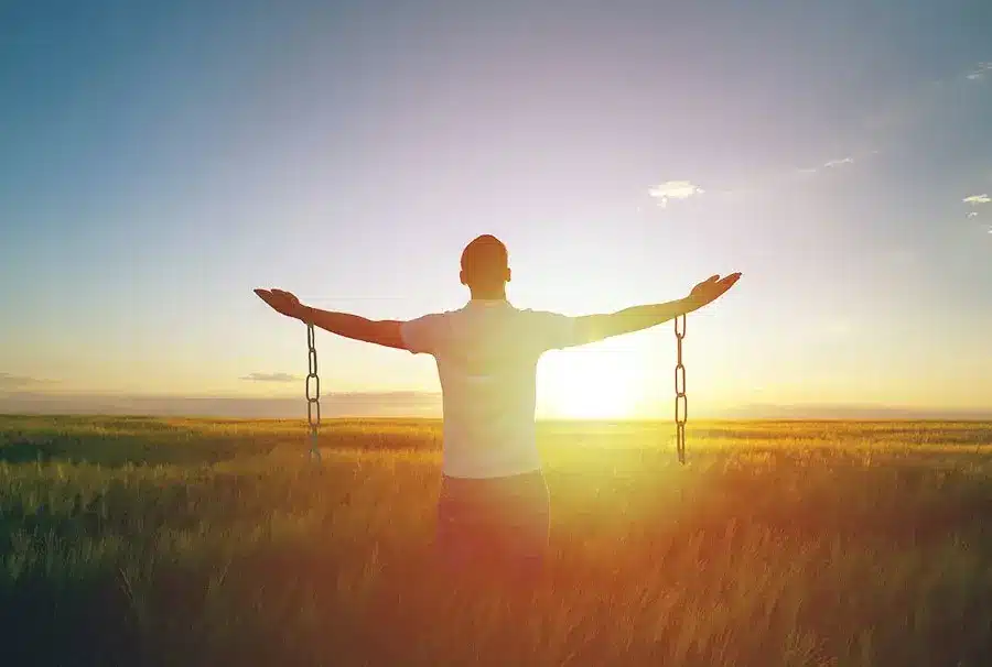 Break black magic, man standing in sunset with arms out and broken chains on his arms.