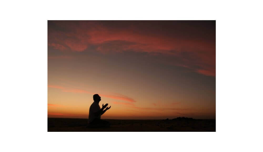 A man's prayer for healing under a sunset.