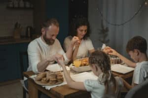 Family sitting around dinner table holding hands doing a spiritual healing prayer.