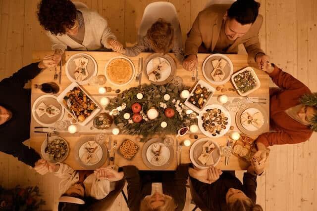 Family sitting around dinner table holding hands doing a spiritual healing prayer.