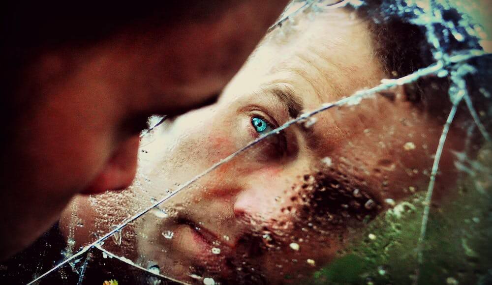 Man looking in broken mirror looking to breaking curses.