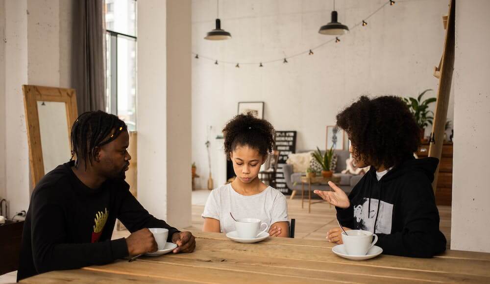 A mother, father and daughter talking about their generational curse at a table.