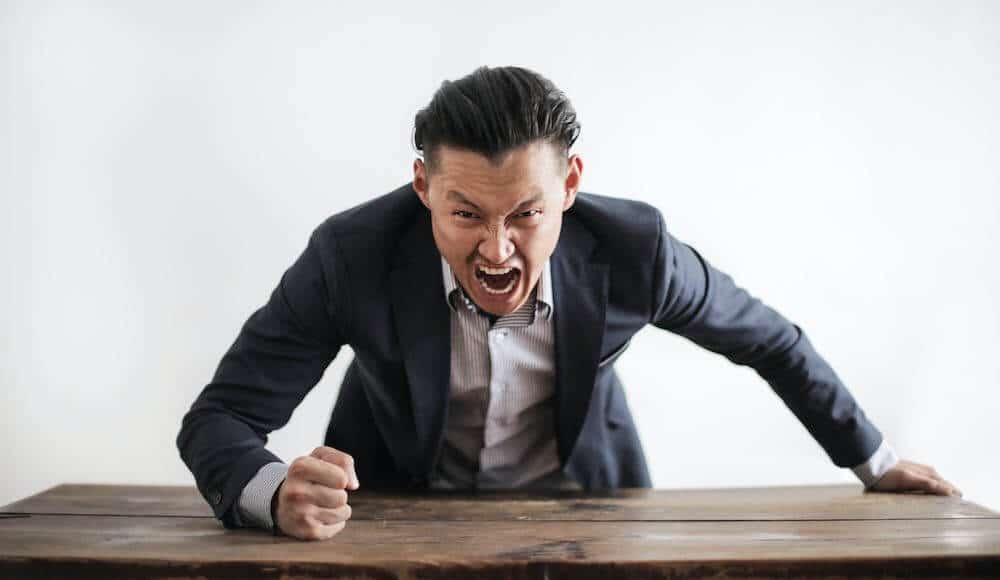 Man pounding his fist on the desk yelling with negative aura symptoms.