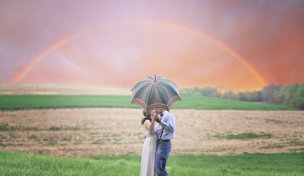 A couple standing under an umbrella and rainbow kissing who learned how to break a love spell.